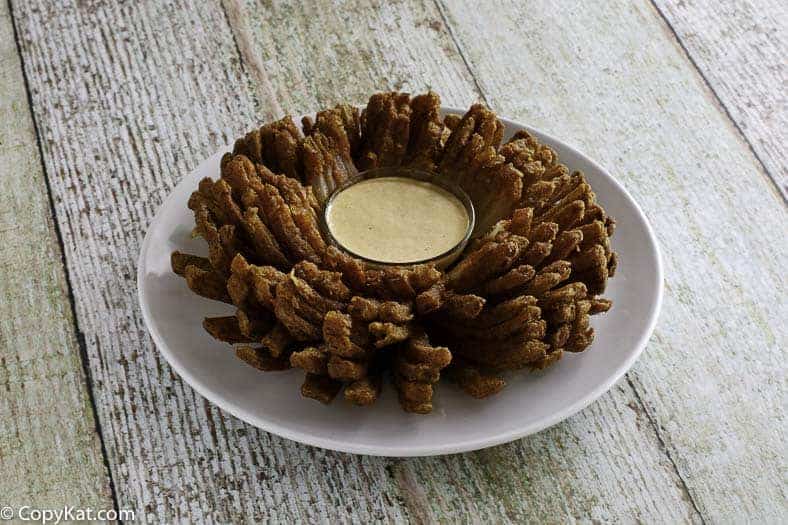 Homemade copycat Steakhouse Bloomin onion on a white plate with dipping sauce.