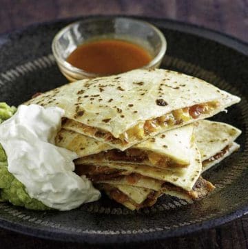 Cheese and bacon quesadilla cut into pieces served with sour cream, guacamole, and sour cream.