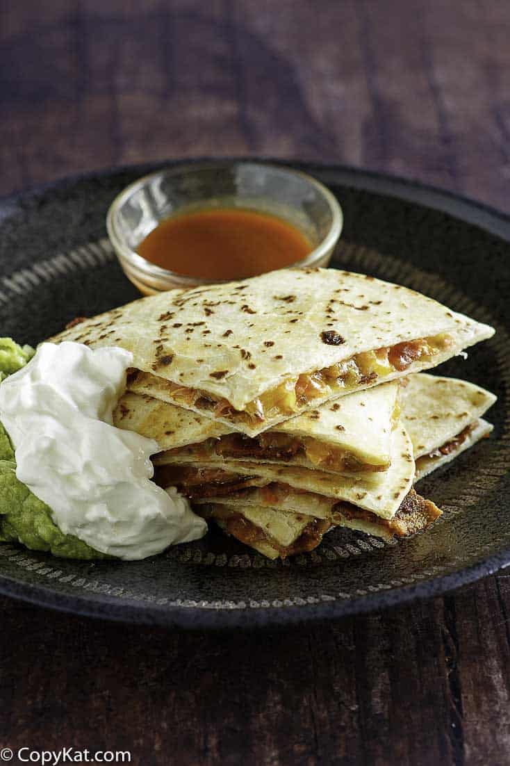 Cheese and bacon quesadilla cut into pieces served with sour cream, guacamole, and sour cream.
