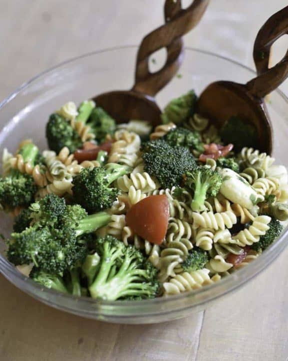 broccoli cheese pasta salad and wood salad tongs in a glass bowl