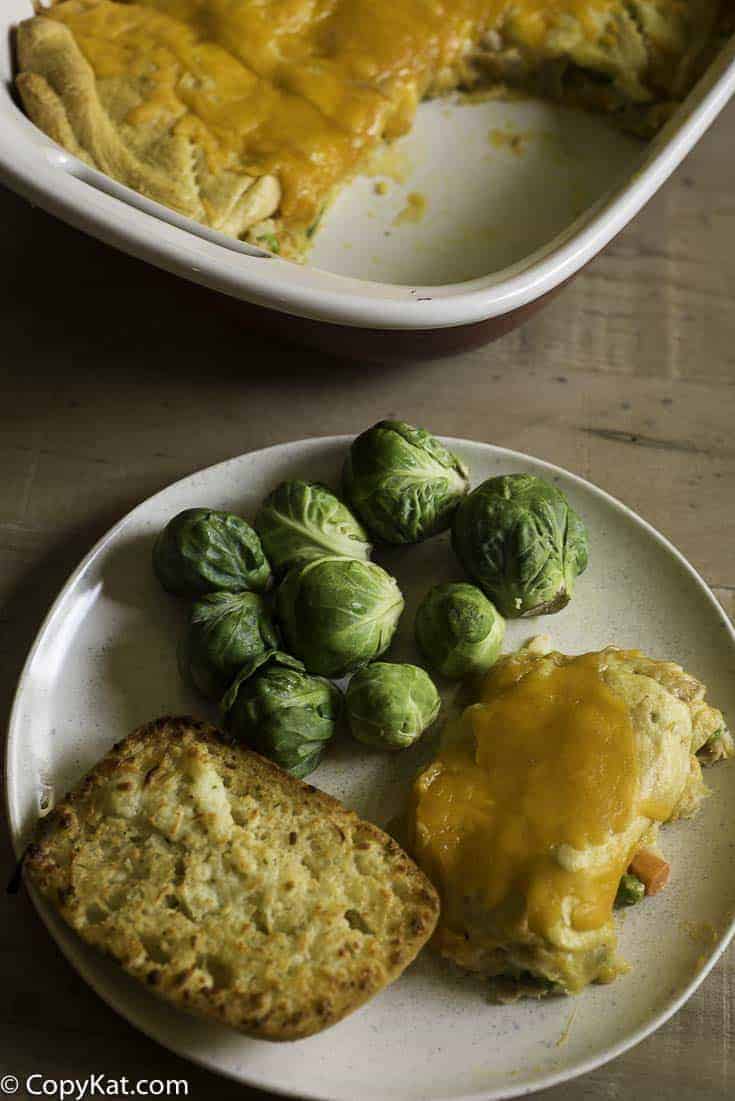 tuna stuffed crescent roll casserole on a plate with garlic bread and Brussels sprouts