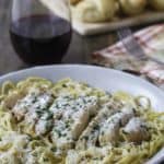 Homemade copycat Olive Garden Grilled Chicken and Alfredo Sauce with Pasta in a bowl next to a glass of red wine.