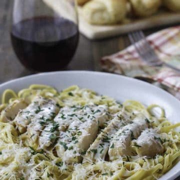 Homemade copycat Olive Garden Grilled Chicken and Alfredo Sauce with Pasta in a bowl next to a glass of red wine.