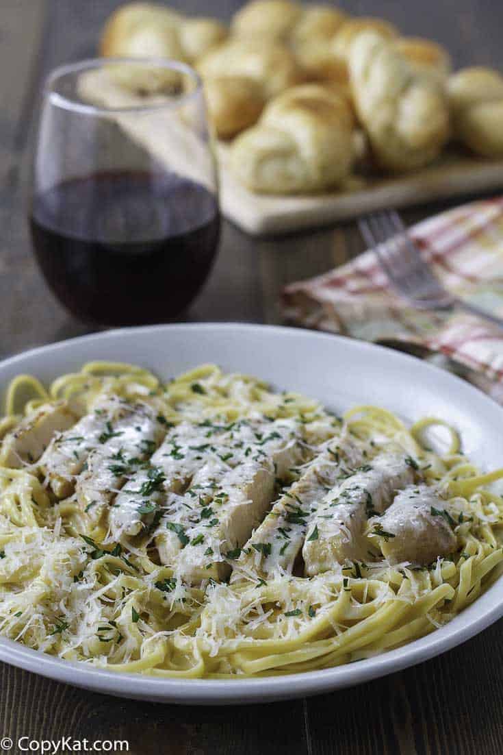 Homemade copycat Olive Garden Grilled Chicken Alfredo Sauce with Pasta in a bowl next to a glass of red wine.