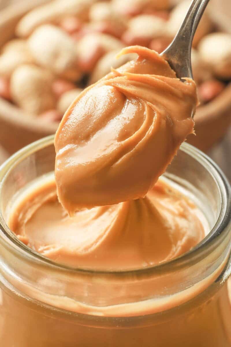 Homemade peanut butter in a spoon and peanuts behind it.