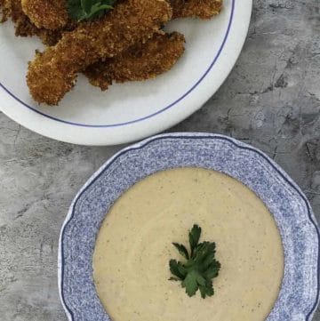 Homemade copycat Raising Cane's dipping sauce in a bowl next to fried chicken tenders on a white plate.