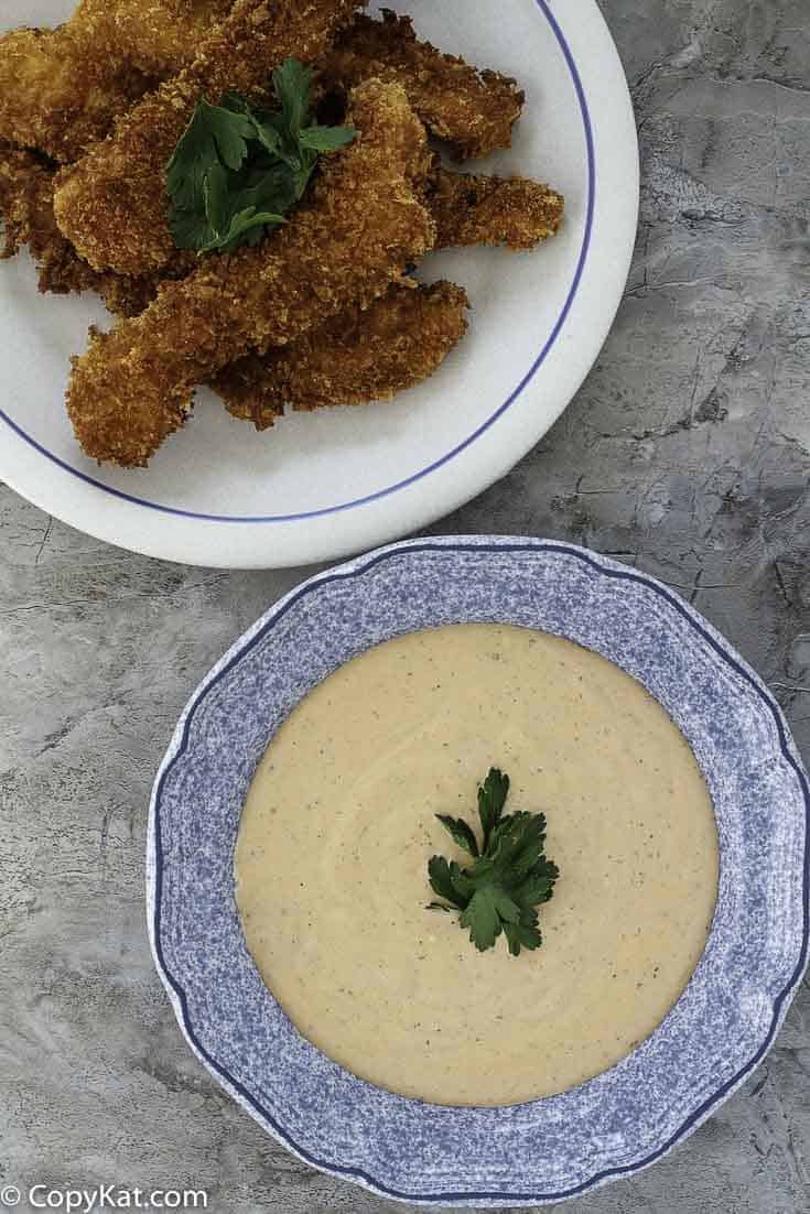 Homemade copycat Raisin Cane's dipping sauce in a bowl next to a plate of fried chicken tenders.