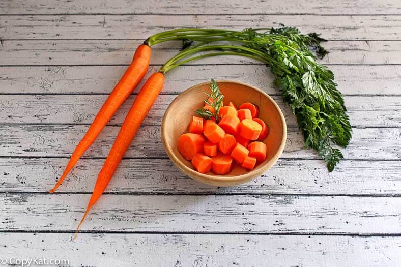 two fresh carrots next to a bowl of cooked carrots