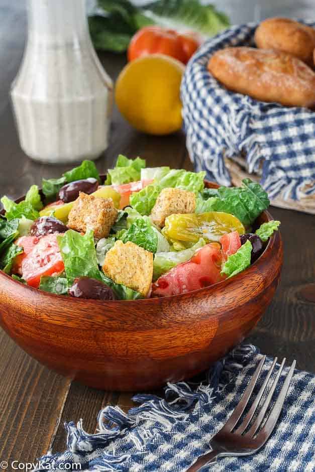 Homemade Italian salad dressing on a salad next to a basket with rolls.. 