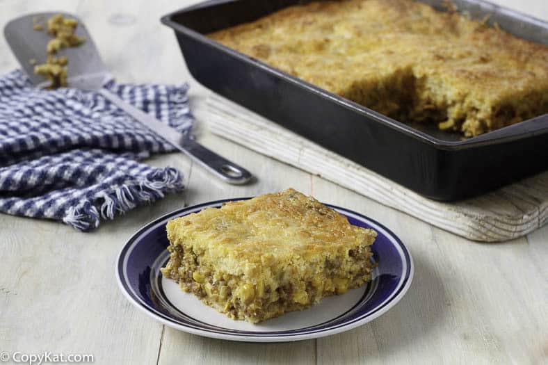 Slice of Mexican cornbread casserole on a plate in front of a pan of it.