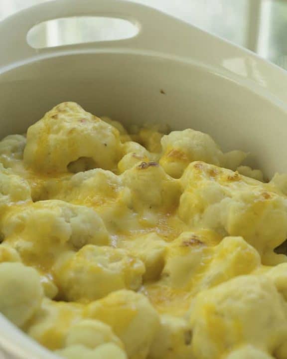 Baked cauliflower with cheddar cheese sauce in a white casserole dish