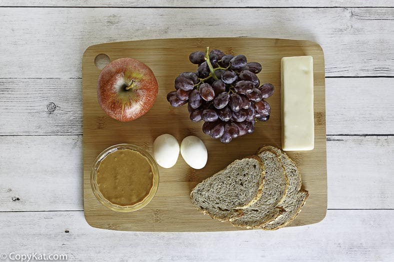 Apple, grapes, eggs, and cheese on a brown cutting board.