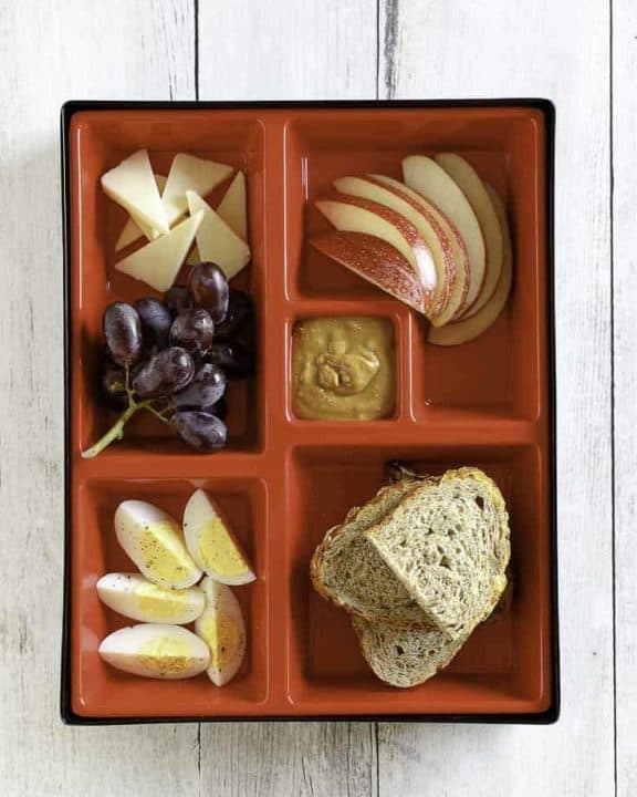 Slices of eggs, cheese, apples, and bread in a red bento box.