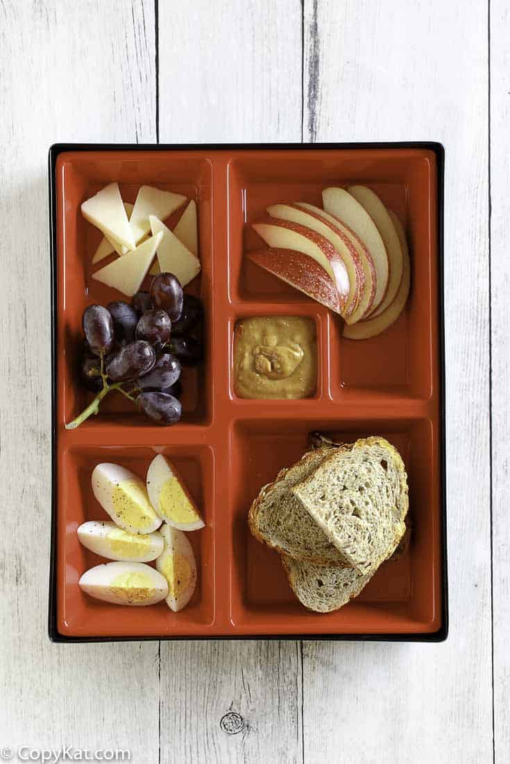 Egg, cheese, apple, and bread slices in a red bento box. 