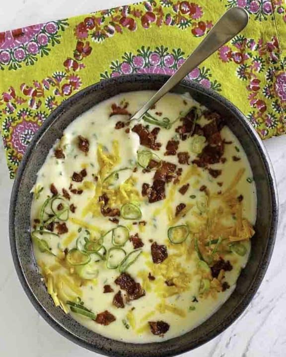 A bowl of baked potato soup topped with cheese, bacon, and green onions.
