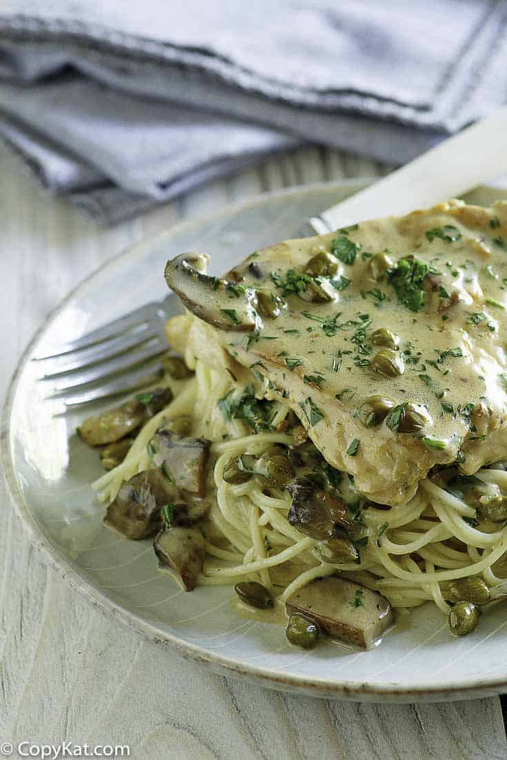 Homemade copycat Cheesecake Factory Chicken Piccata with pasta on a plate with a fork.