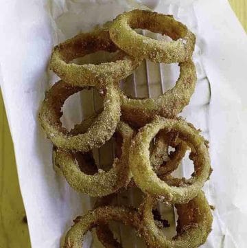 Homemade Sonic Onion Rings and dipping sauce on parchment paper in a metal serving basket.