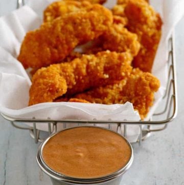 Homemade Red Robin Campfire Sauce in a ramekin in front of a basket of chicken tenders.