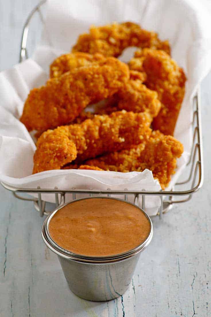 Homemade Red Robin Campfire Sauce in a ramekin in front of a basket of chicken tenders.