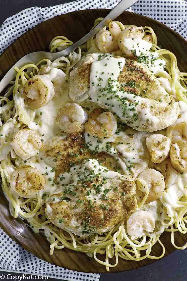 Homemade copycat Outback Steakhouse Queensland Chicken and Shrimp pasta and a fork in a brown wood bowl.