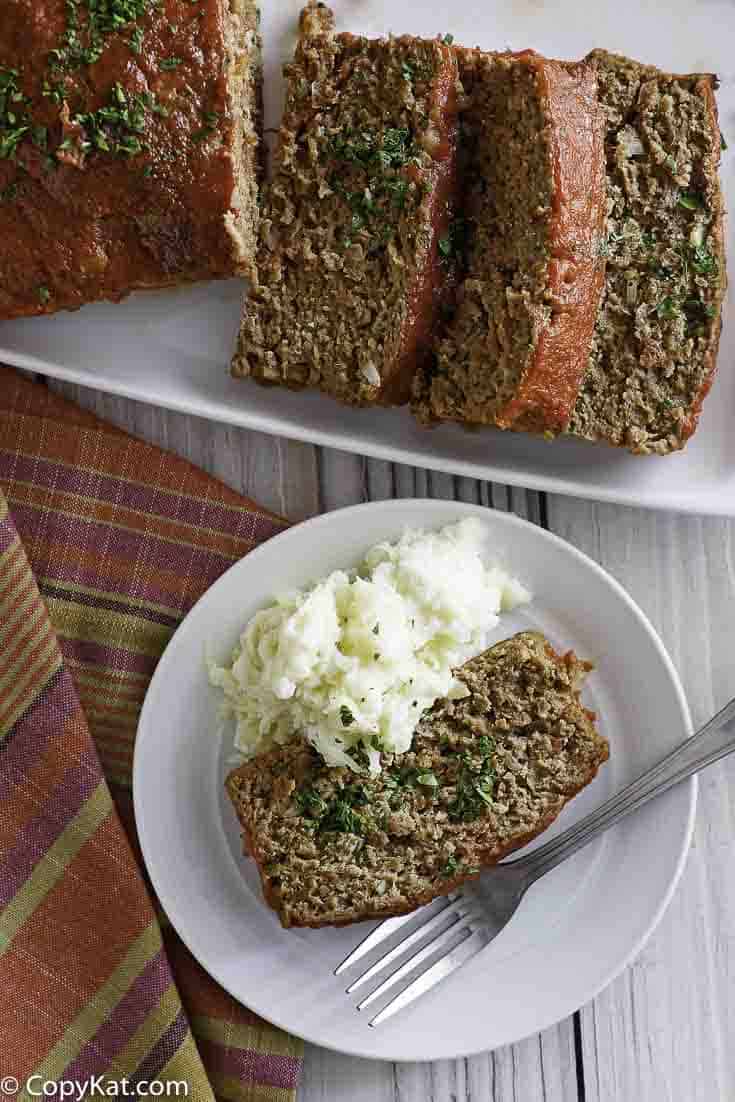 Homemade Boston Market Meatloaf on a serving dish and plate with mashed potatoes.