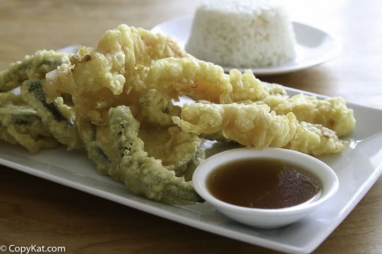 Vegetables fried in tempura batter and dipping sauce on a plate.