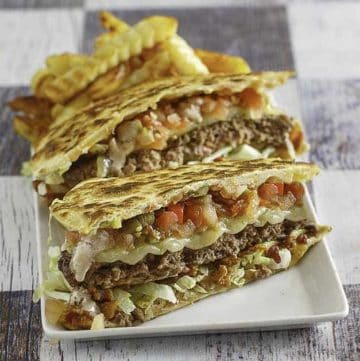 A quesadilla cheeseburger cut in half on a plate with french fries