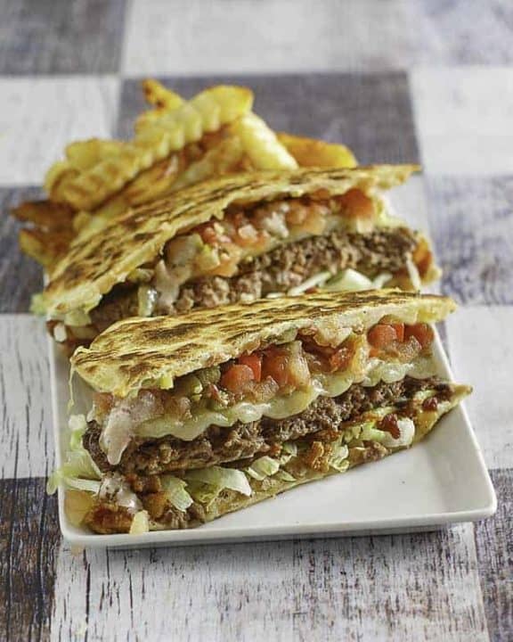 A quesadilla cheeseburger cut in half on a plate with french fries