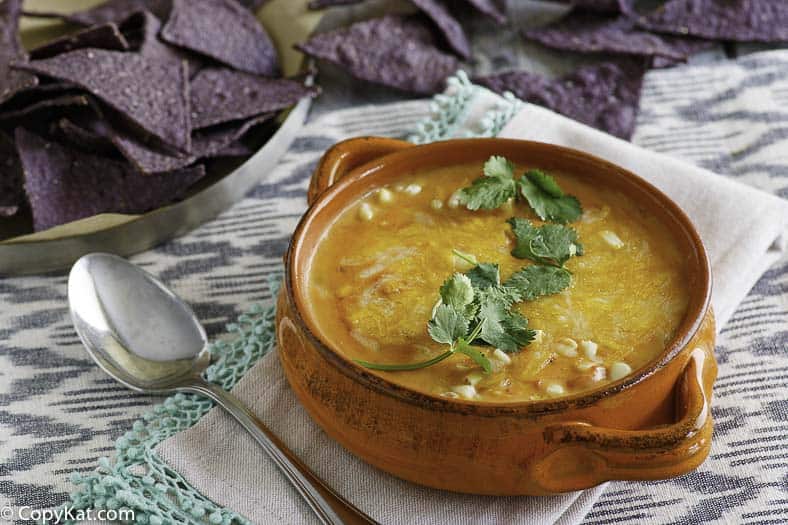 Bowl of white corn tortilla soup garnished with cilantro and blue corn tortilla chips. 