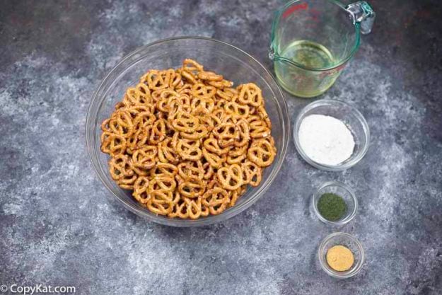 A bowl of pretzels, dry ranch salad dressing mix, garlic powder, vegetable oil, and dill weed.