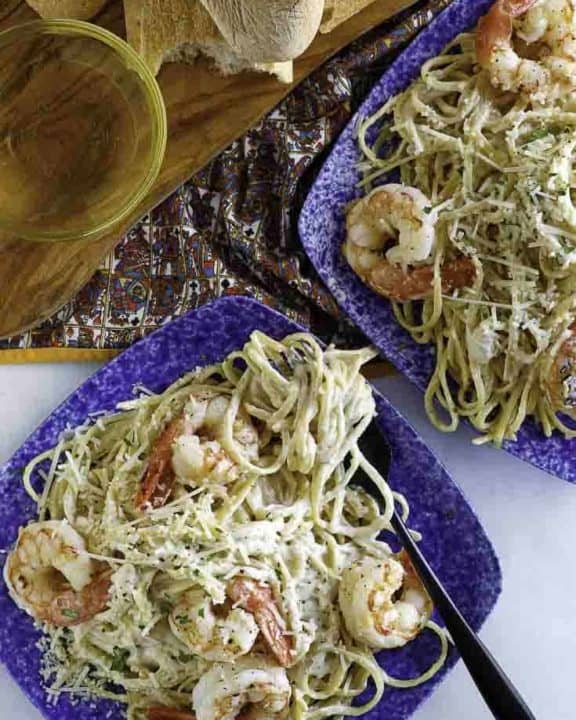 Two plates of homemade copycat Olive Garden shrimp alfredo being served with bread.