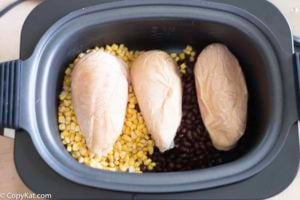A crockpot with black beans, corn, and frozen chicken breasts.
