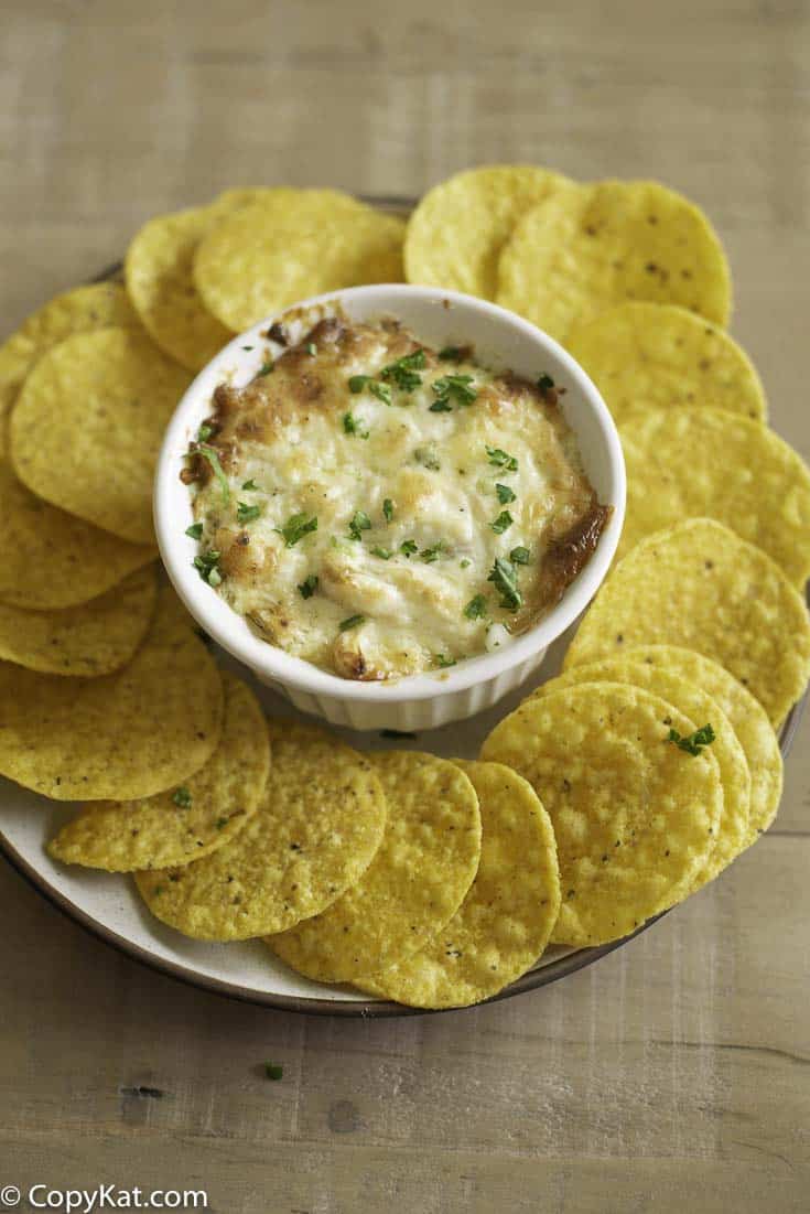 A bowl of hot crab dip with corn chips on a platter