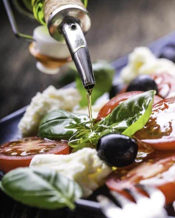 A plate of fresh mozzarella, tomatoes, basil leaves, and olive oil