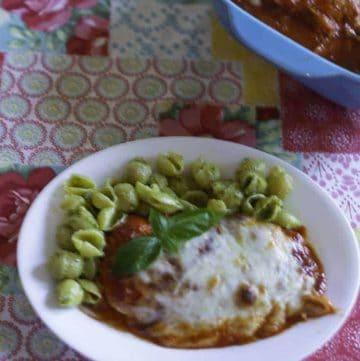 Baked chicken parmesan with cheese served with pesto pasta.