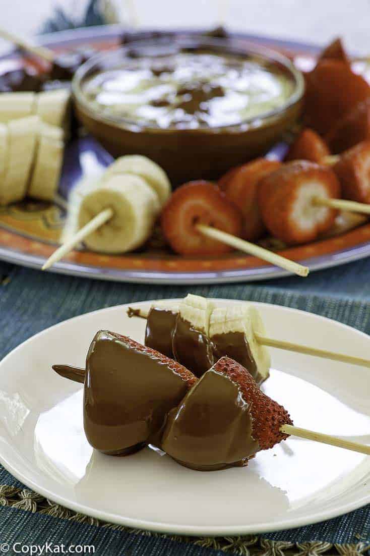 Skewers of fruit dipped in homemade Melting Pot chocolate fondue on a plate.