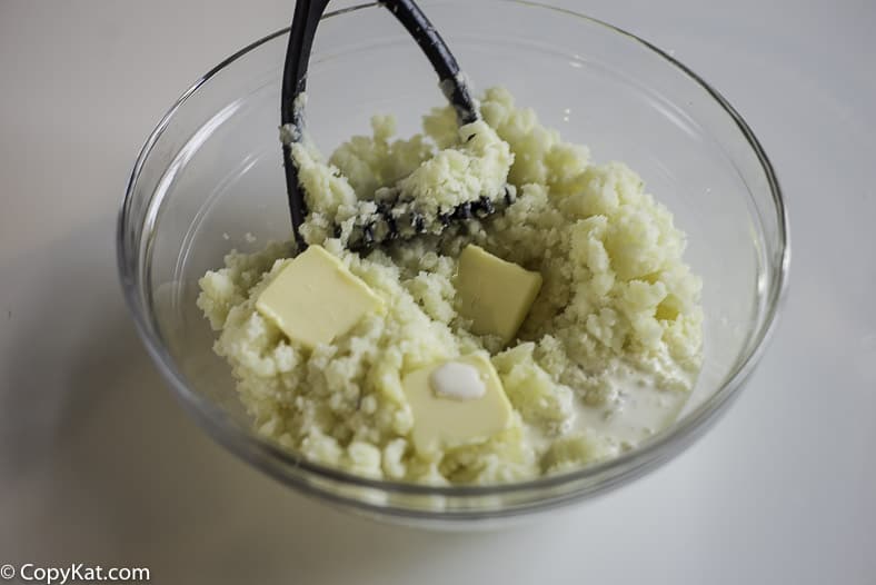 a bowl of potatoes getting mashed with butter, cream, and salt 