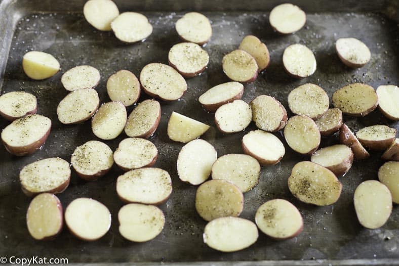 Cut red new potatoes with seasoning and oil on a baking sheet.