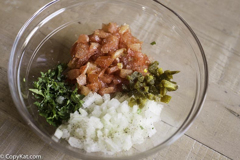 a mixing bowl with finely chopped onions, tomatoes, cilantro, jalapenos, and salt