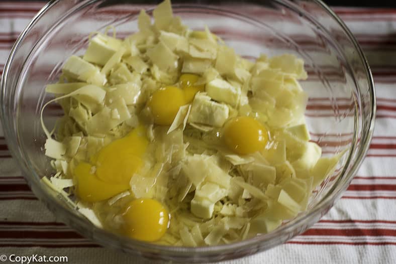 combining spaghetti, eggs, and cheese in a bowl