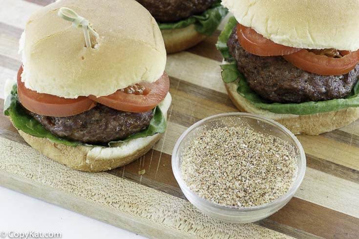 homemade burger seasoning next to hamburgers on a wood cutting board.