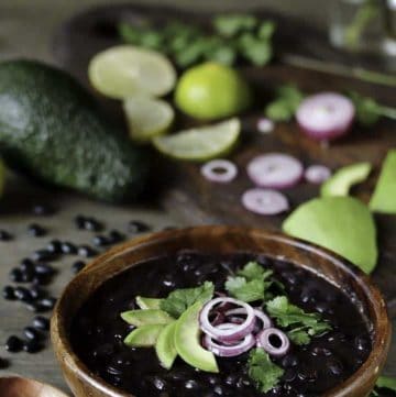 a bowl of cooked black beans with cilantro, lime, red onion and avocado.