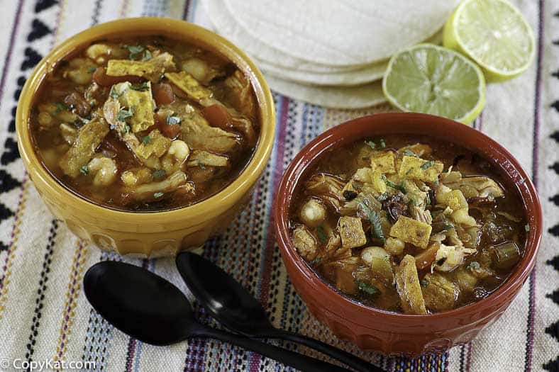 two bowls of spicy chicken soup with tortilla strips and lime