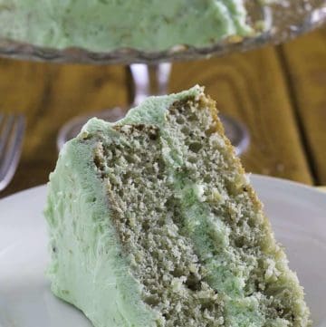 A slice of pistachio cake on a plate with the cake in the background.