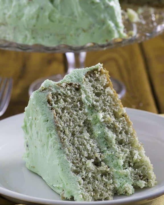 A slice of pistachio cake on a plate with the cake in the background.