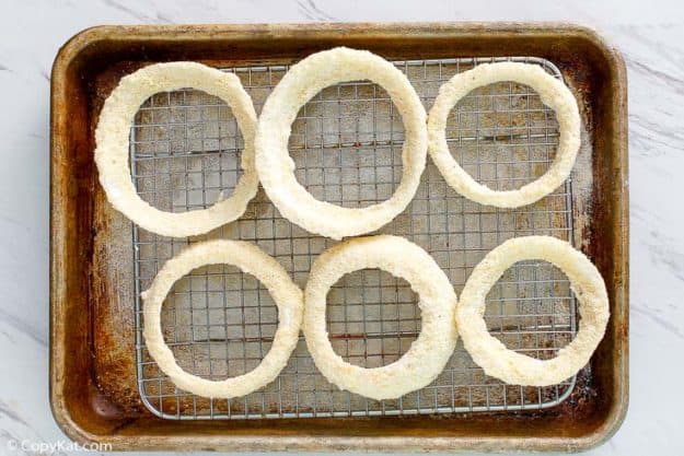 battered onion rings on a wire rack before frying