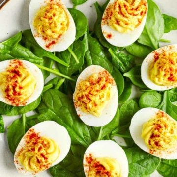 a plate of deviled eggs on top of fresh spinach leaves