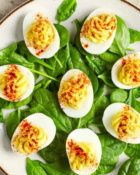 a plate of deviled eggs on top of fresh spinach leaves