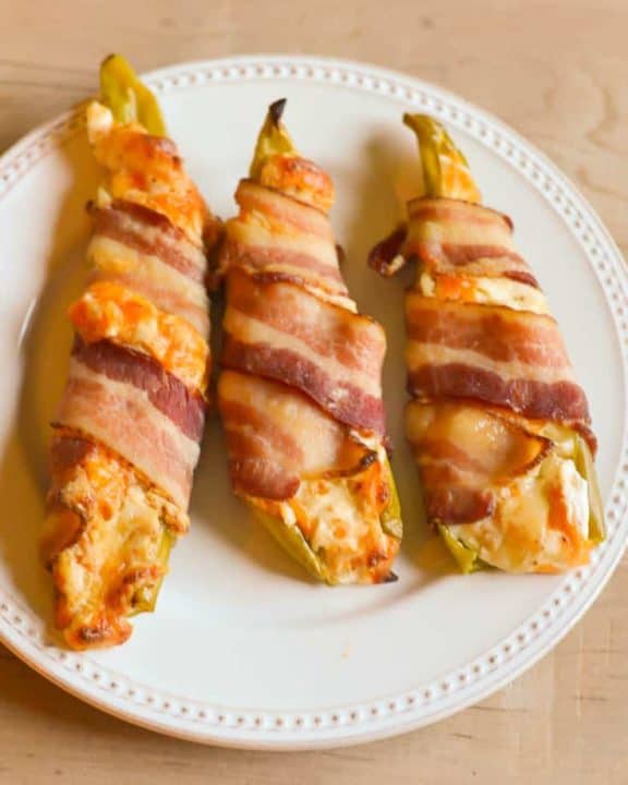 three bacon wrapped stuffed hatch chile peppers on a plate