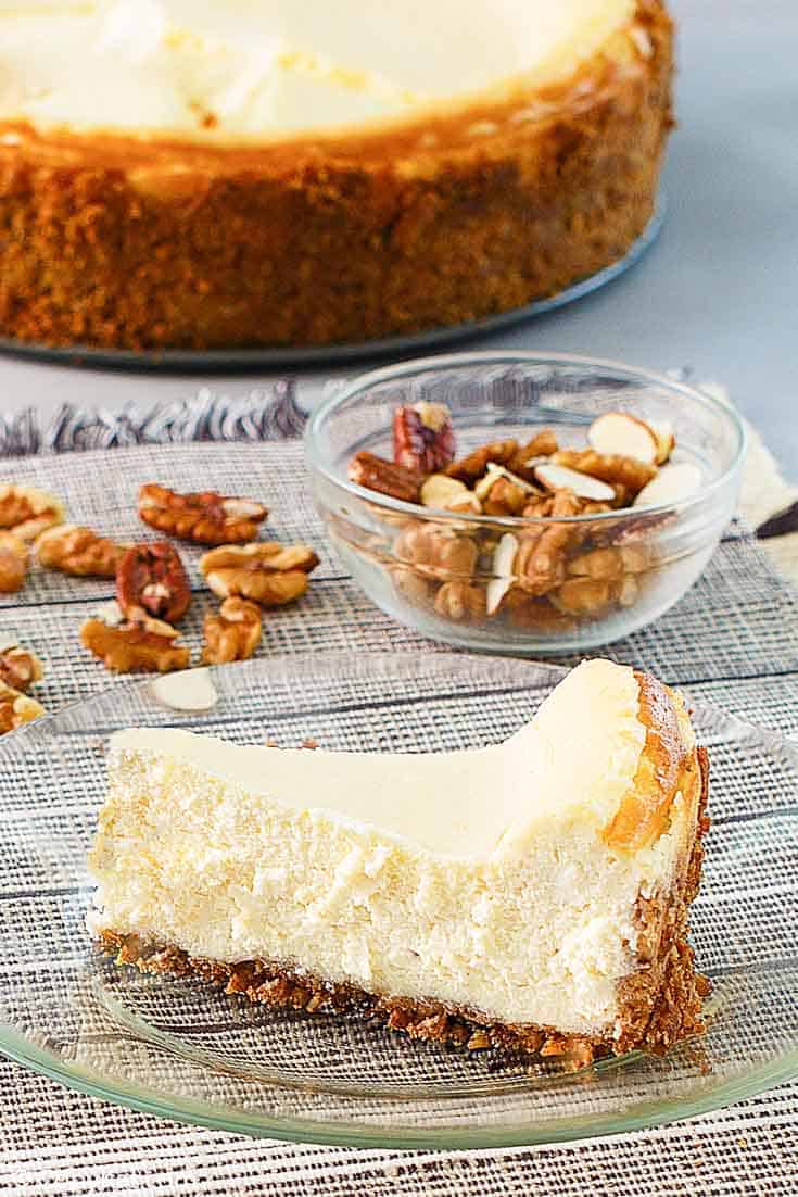a slice of cheesecake, nuts, and a cheesecake on platter